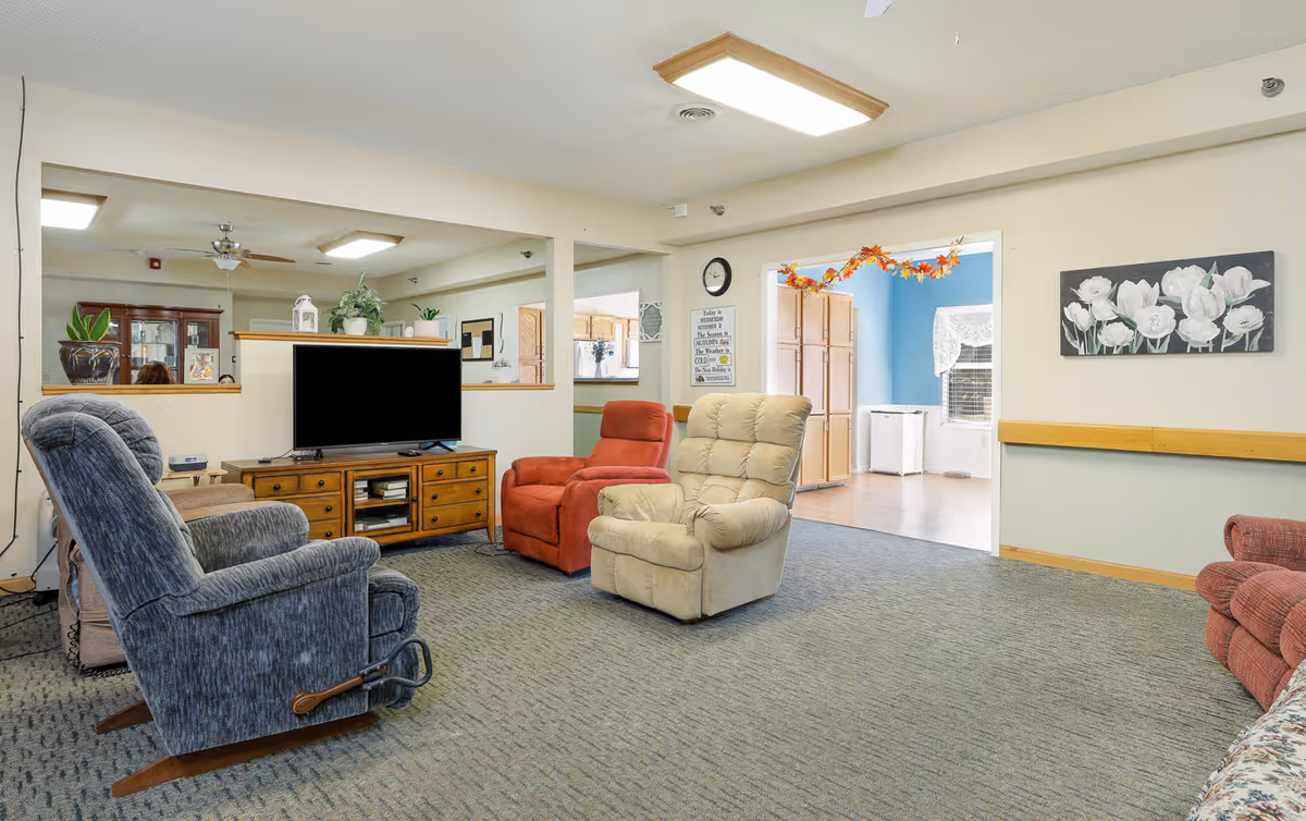 Communal lounge with several recliners arranged around a television on a wooden console.