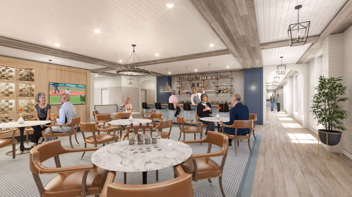 Spacious dining and lounge area with round marble-topped tables, leather chairs, a bar in the background, and residents seated and conversing.
