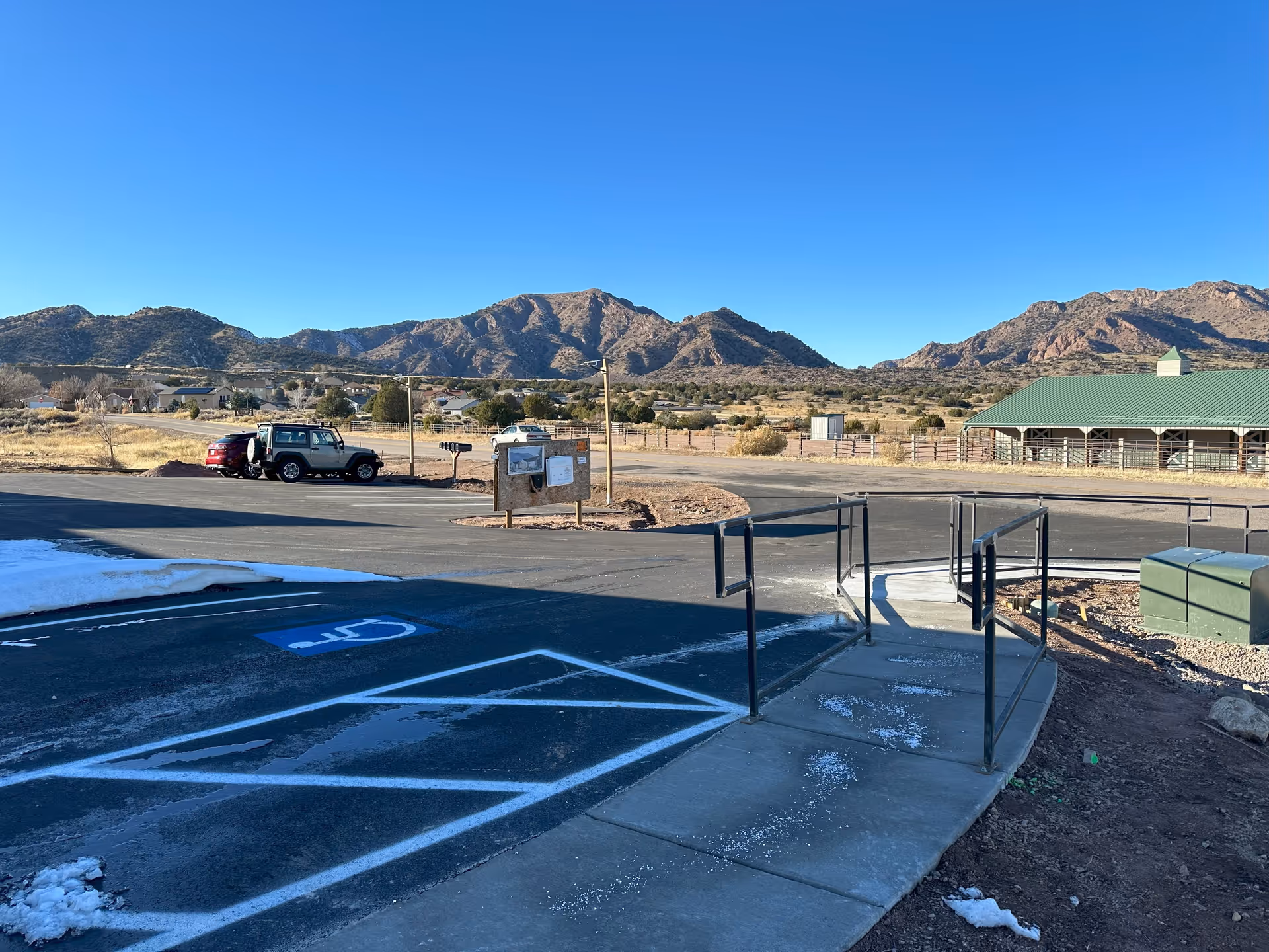 Parking lot with accessible ramp and marked handicap spaces in front of a mountain landscape and a green-roofed building.