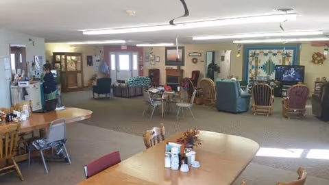 Spacious senior living common area with tables, chairs, and comfortable lounge seating.