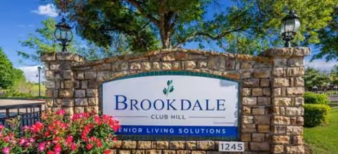 Stone entrance sign for Brookdale Club Hill Senior Living Solutions amid landscaped greenery.