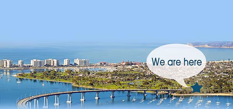 Aerial view of a coastal town and marina with a curved bridge and a speech bubble reading "We are here".