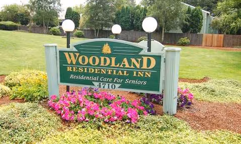 Exterior view of Woodland Residential Inn sign amid colorful flowers and a green lawn.