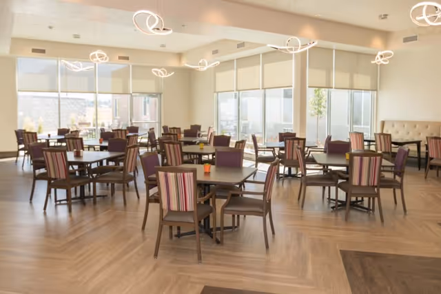 Spacious bright dining room with multiple square tables and striped upholstered chairs and modern pendant lights.