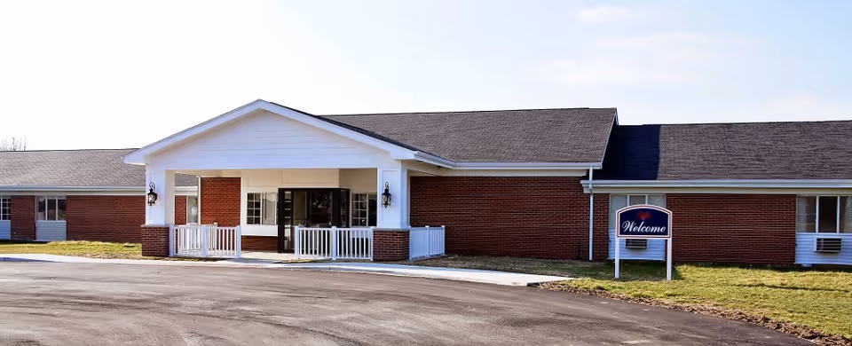 Brick single-story senior living facility front entrance with a covered portico and a 'Welcome' sign on the lawn.