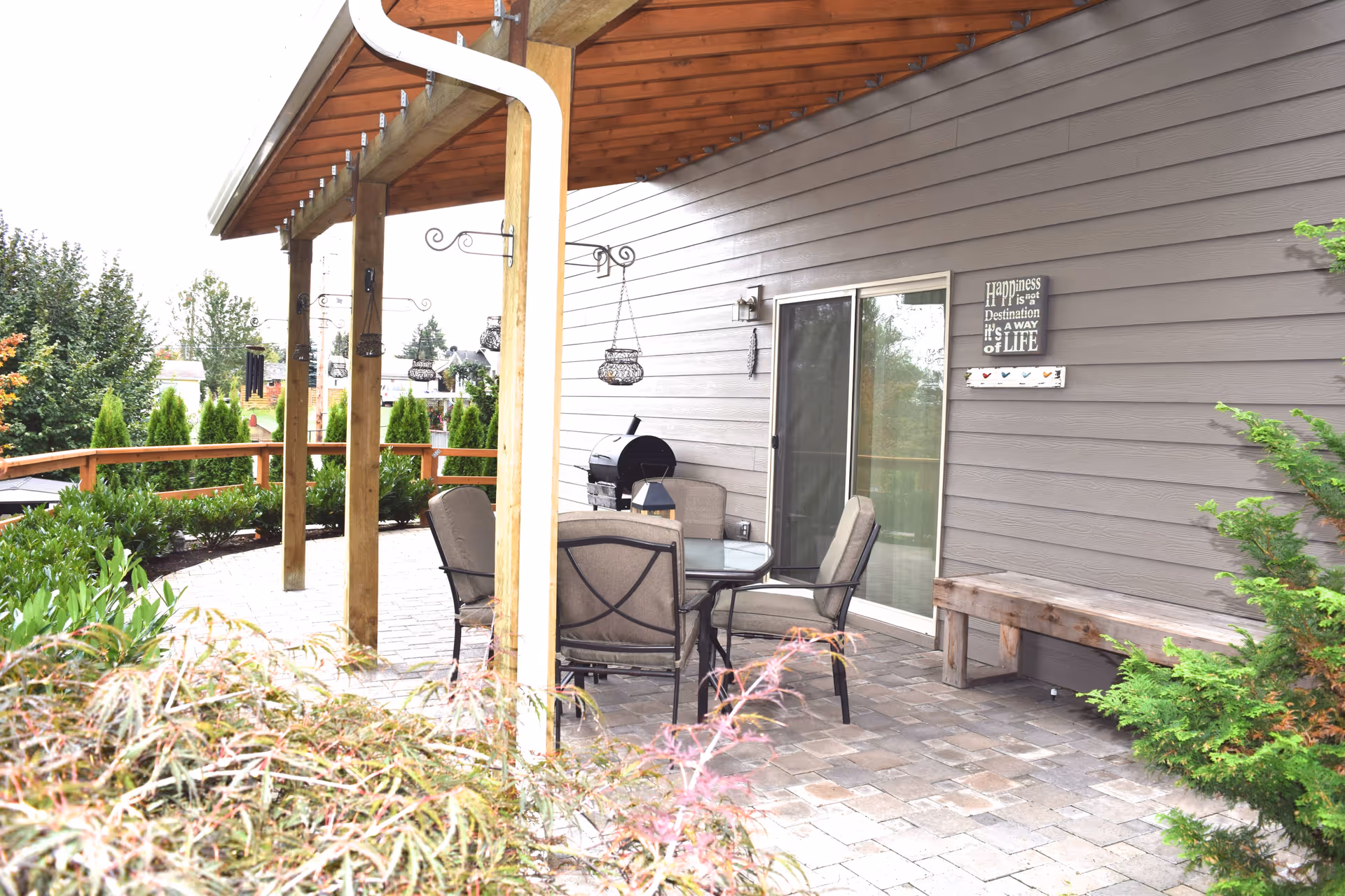 Covered outdoor patio with a table and chairs, a grill, and sliding glass door against house siding.