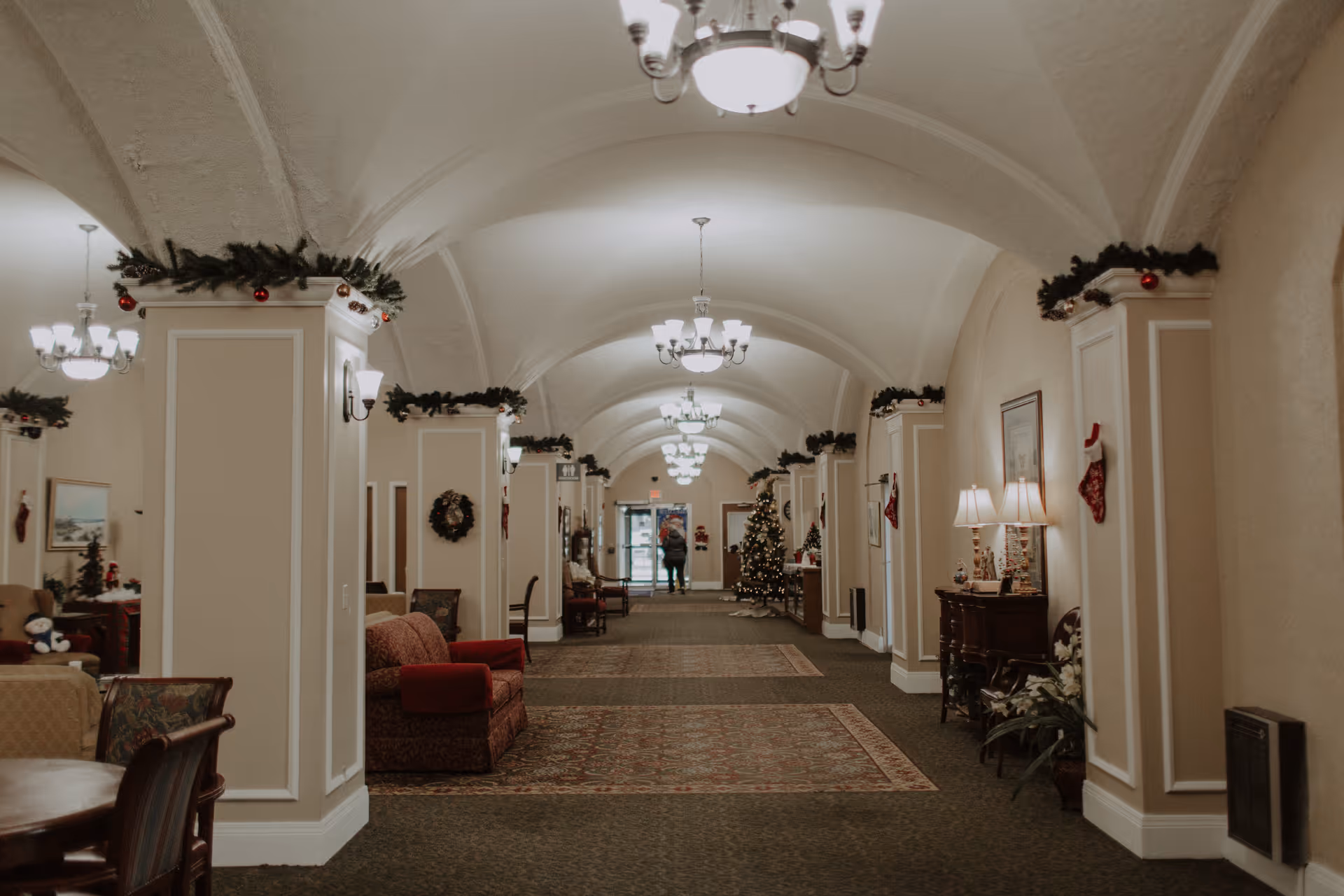 Long decorated hallway/lobby with arched ceilings, chandeliers, seating areas and Christmas decorations.