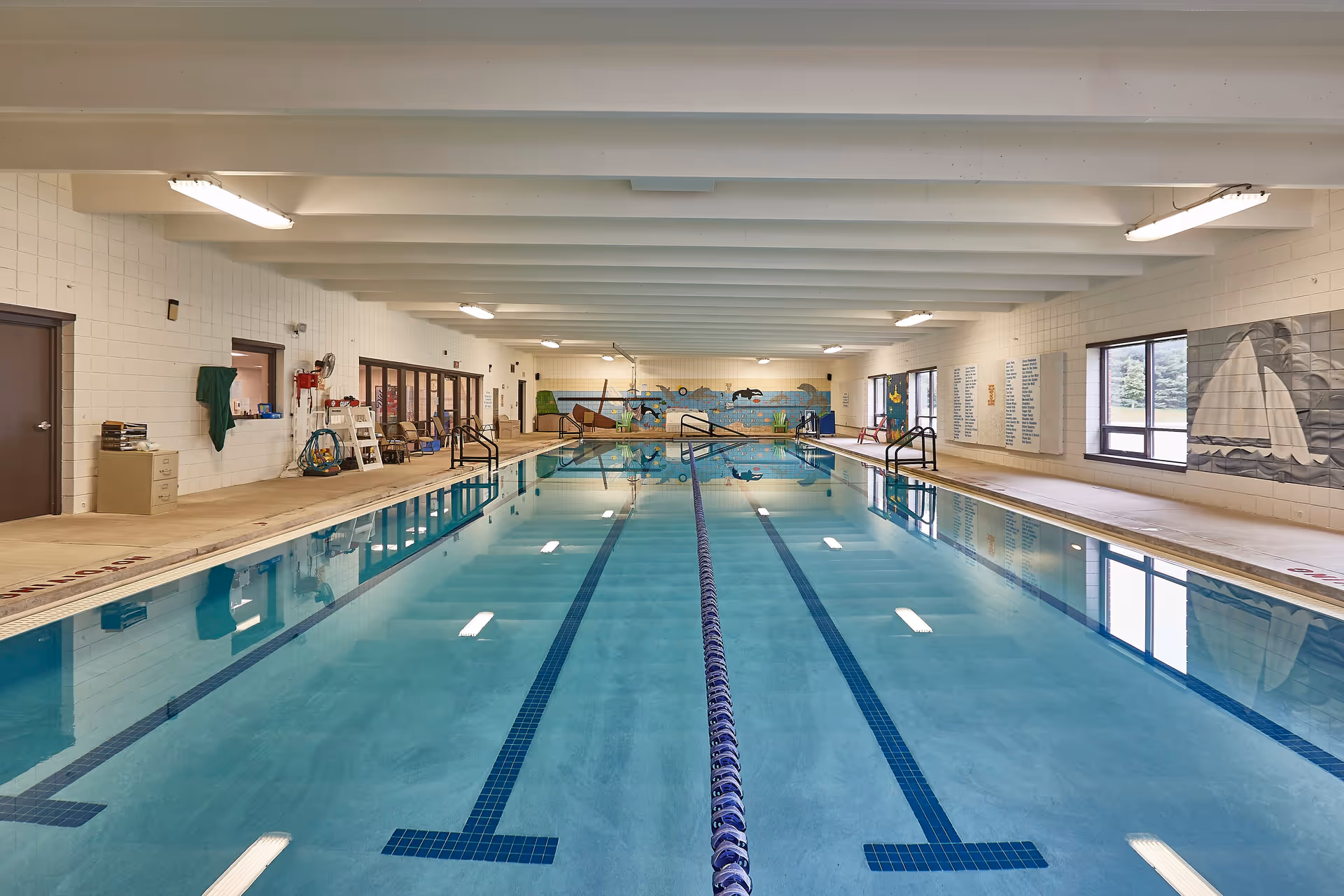 Indoor swimming pool with lap lanes, pool deck, windows and a mural on the far wall.