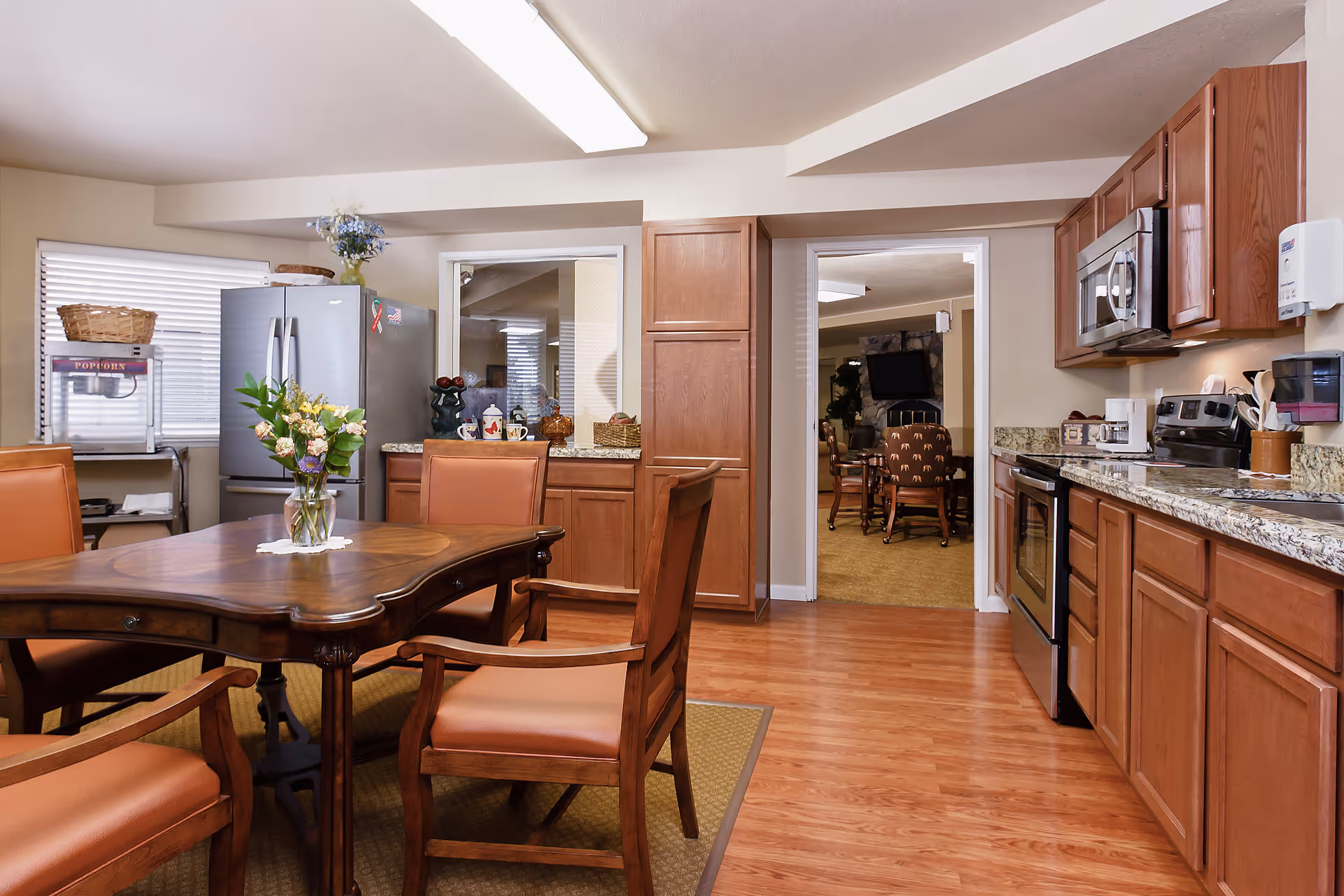 A bright combined kitchen and dining area with a wooden table and chairs, stainless refrigerator, wooden cabinets, and appliances.