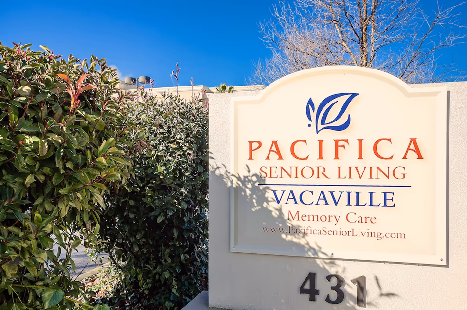Outdoor sign for Pacifica Senior Living Vacaville Memory Care with greenery and a clear blue sky in the background.