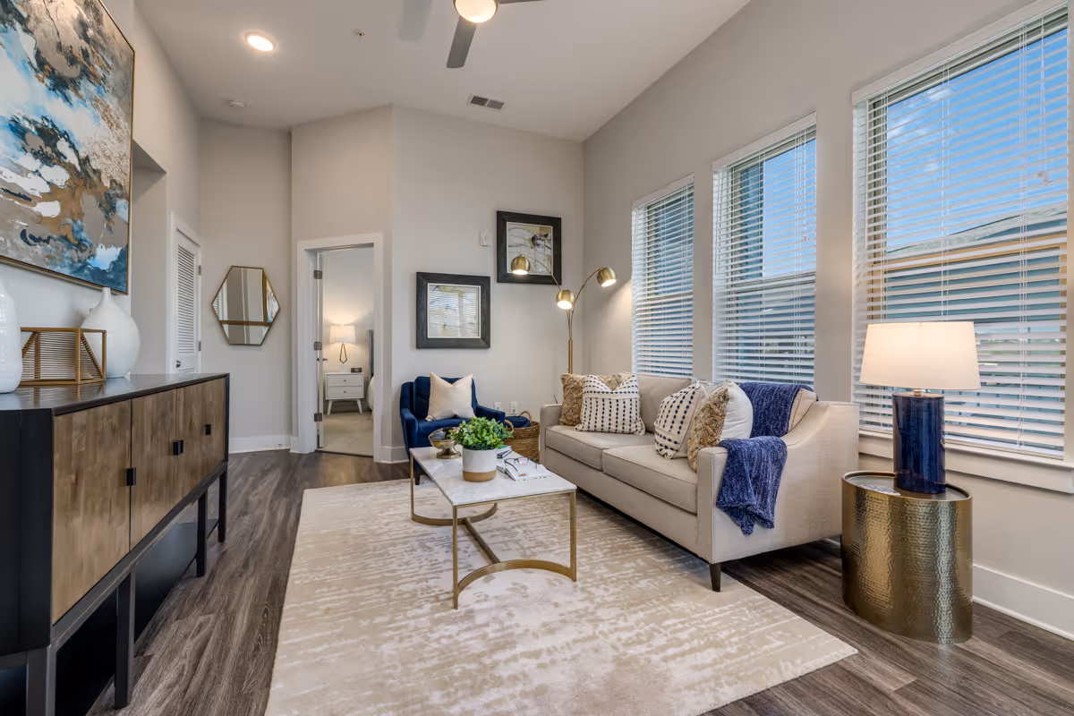 Bright modern living room with a sofa, armchair, coffee table, sideboard, and large windows.