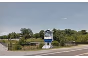 Roadside sign for North Roanoke Assisted Living on a grassy, fenced lot with trees under a blue sky.