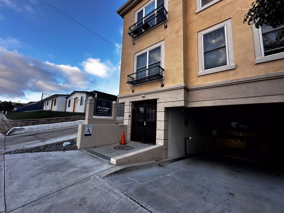 Entrance and garage of a multi-story yellow apartment building with an 'Ivy Park at La Jolla' sign and driveway.