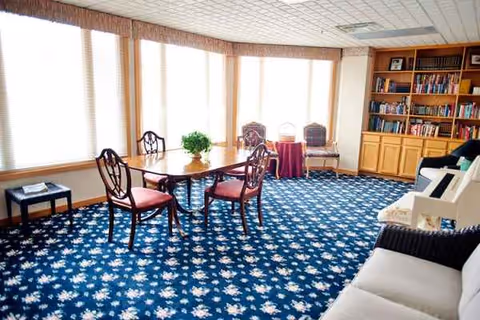 Bright interior lounge featuring a round table, chairs, bookshelf, plants, and a white sofa.
