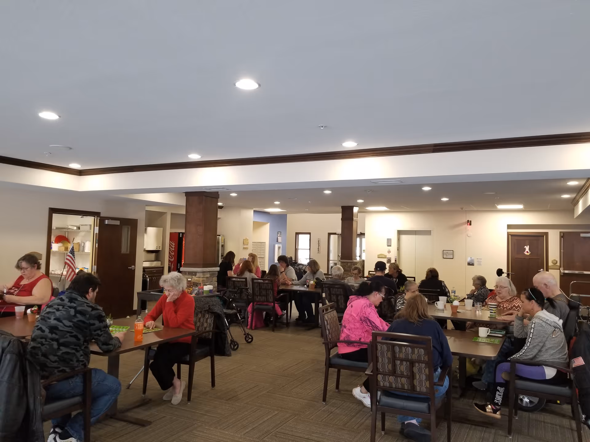 Residents of a senior living facility engaged in activities at tables in a communal dining area.
