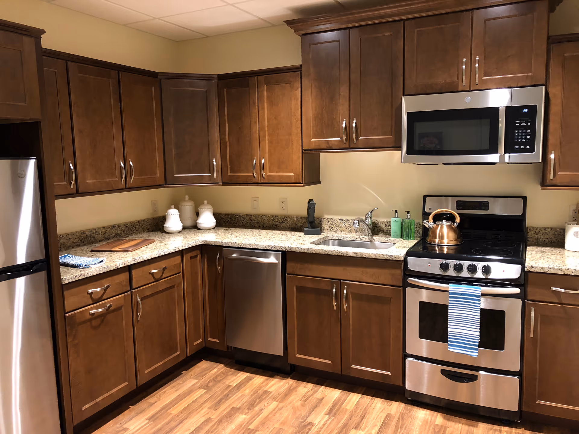 Modern kitchen with wooden cabinets, granite countertops, and stainless steel appliances including a refrigerator, dishwasher, microwave, and stove.