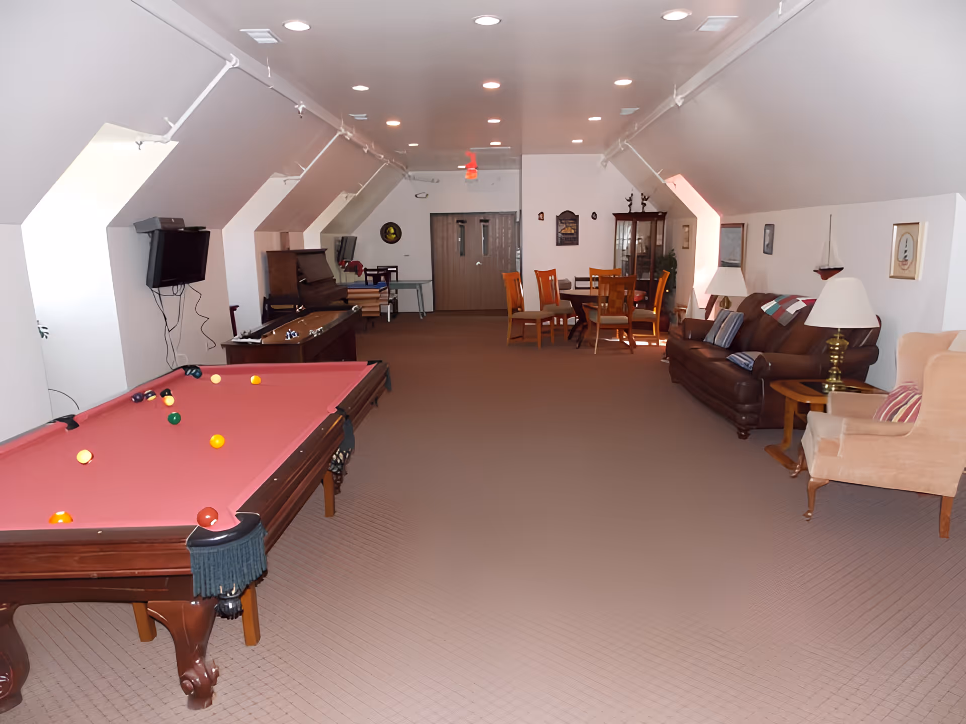 Large recreational lounge with a pink-felt pool table, seating area with sofas and chairs, and a dining table at the far end.
