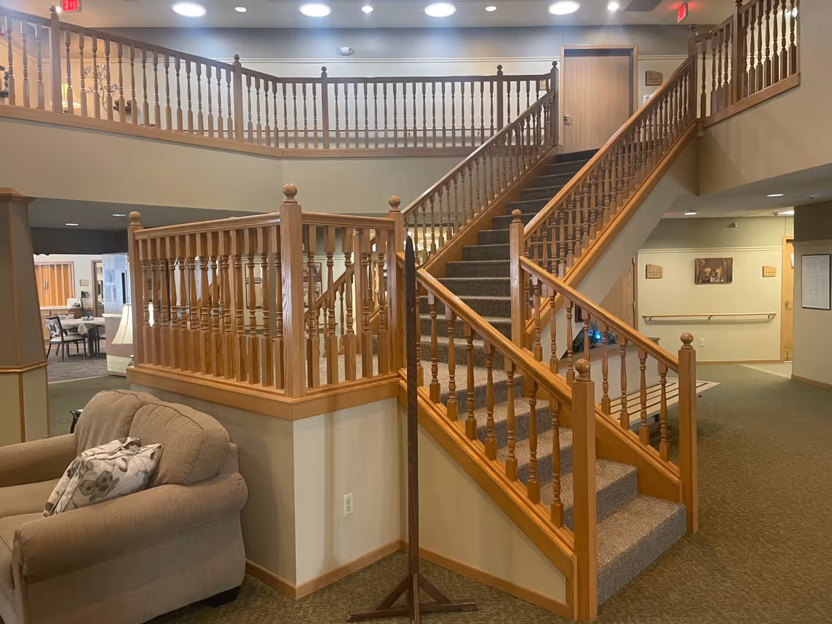 Interior common area with a central carpeted staircase and wooden railings overlooking a seating area.