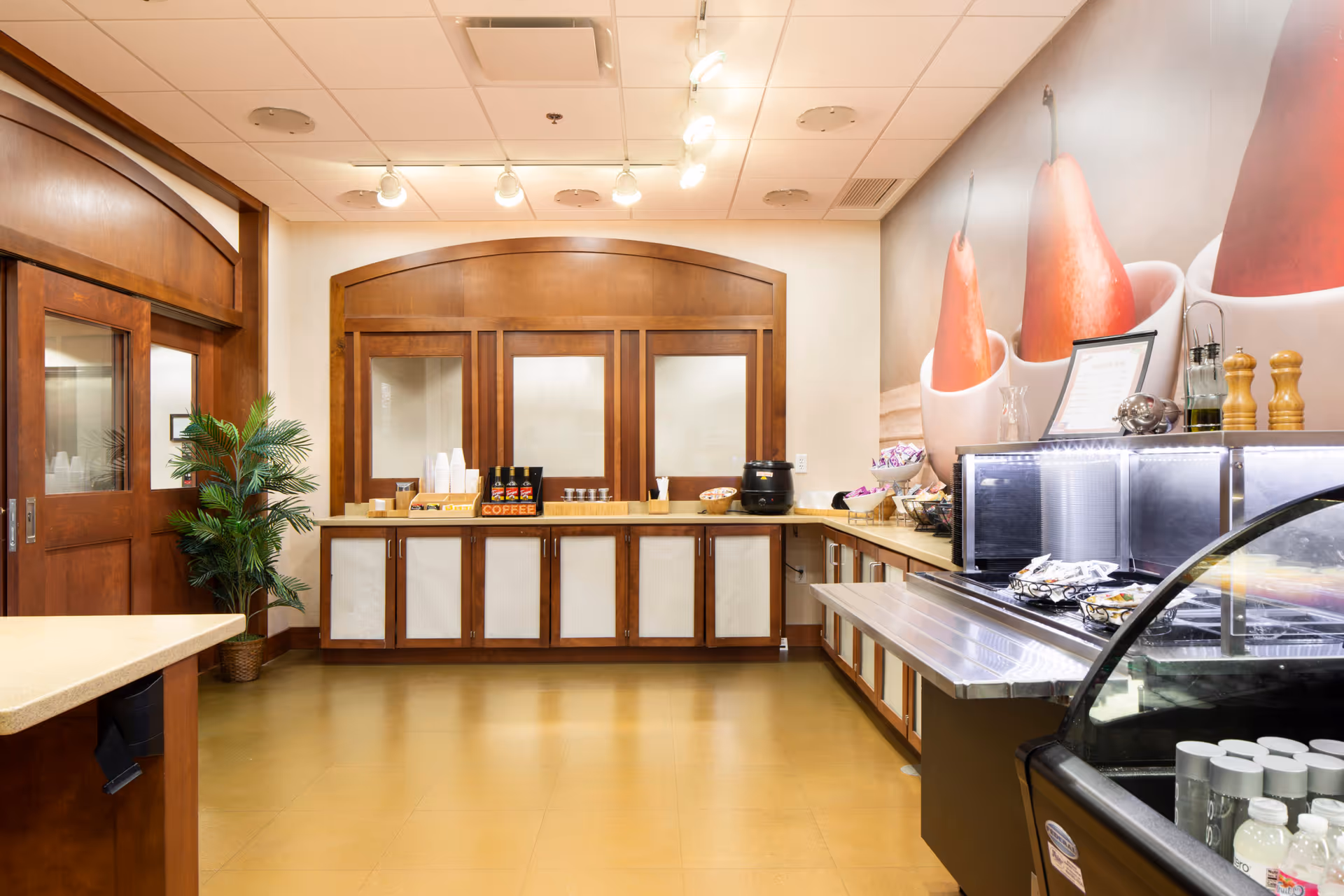 A bright serving area with wooden cabinets, a coffee station, refrigerated display case and countertop service area.