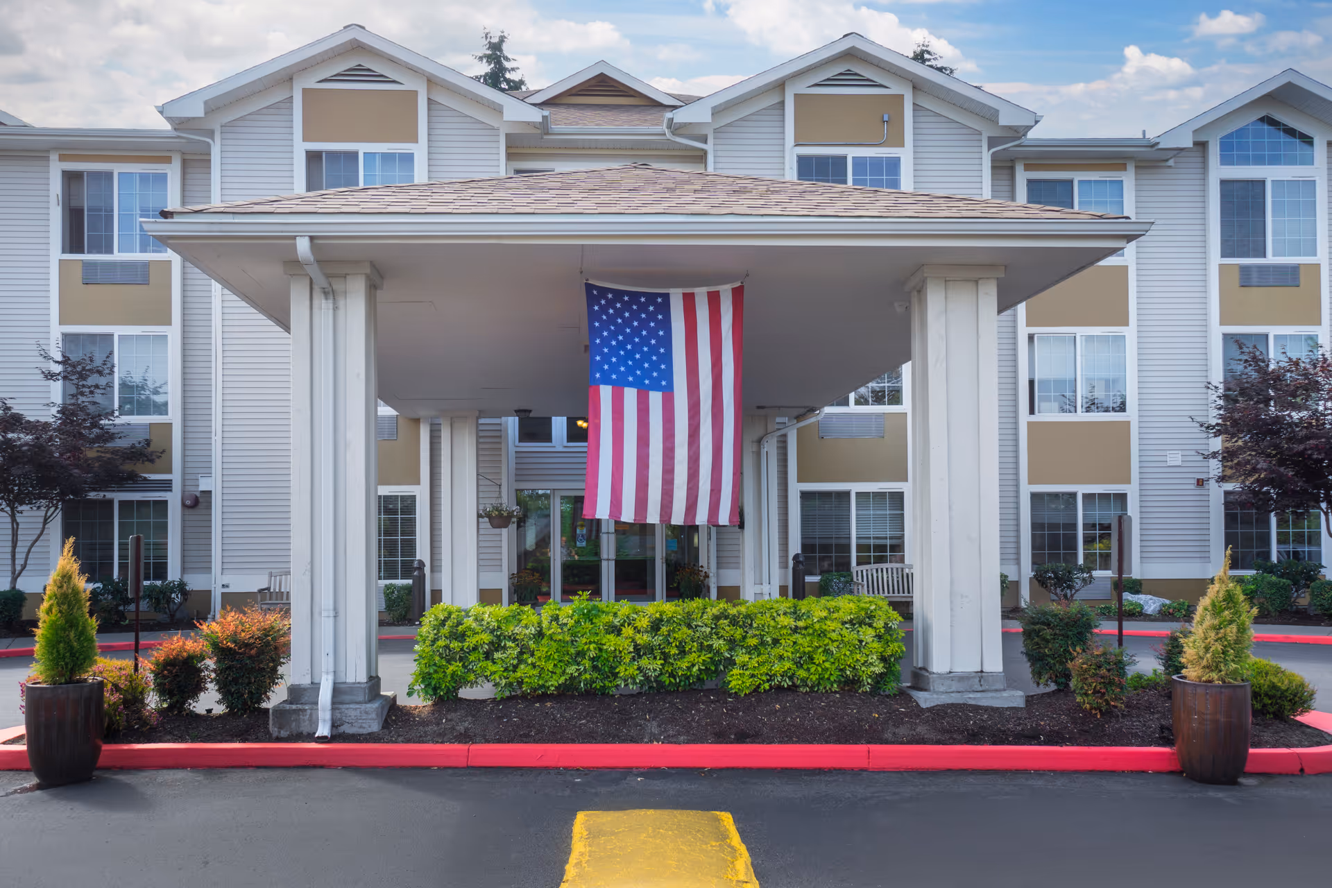 Front view of a multi-story senior living building with a covered entrance and American flag.
