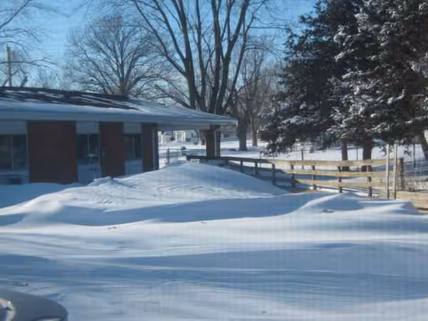 Snow-covered nursing home exterior with a fence and bare trees.