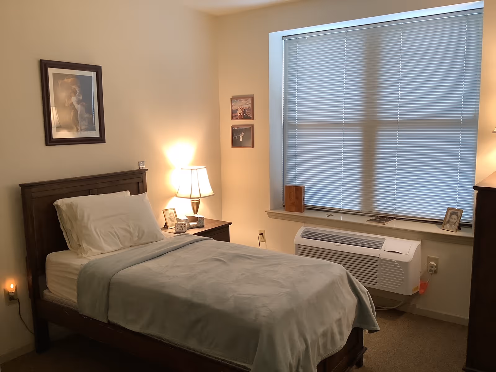 A cozy bedroom with a single bed, lamp, and photographs on the wall.