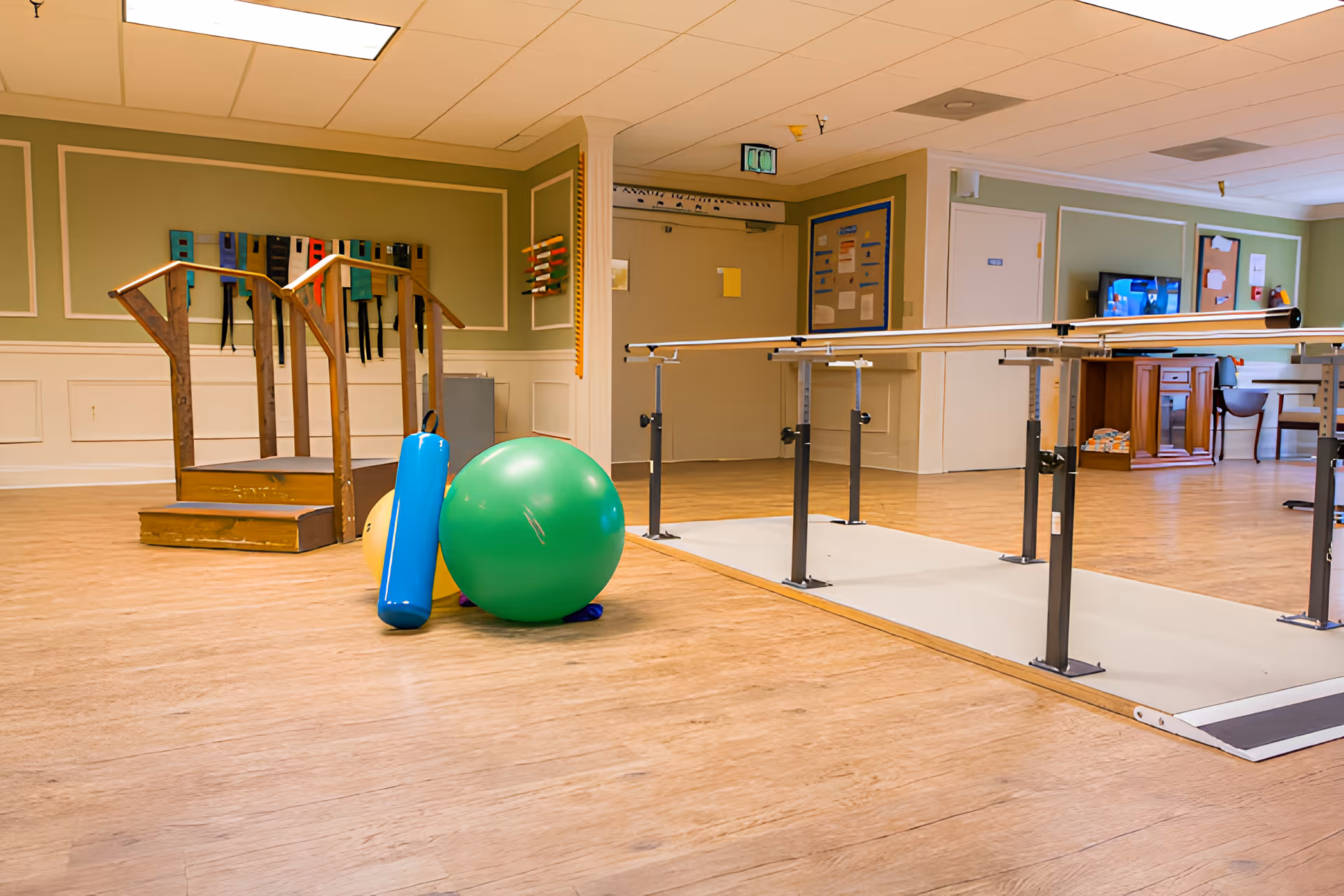Rehabilitation room in a nursing center with parallel bars, exercise balls, and wooden step stairs.