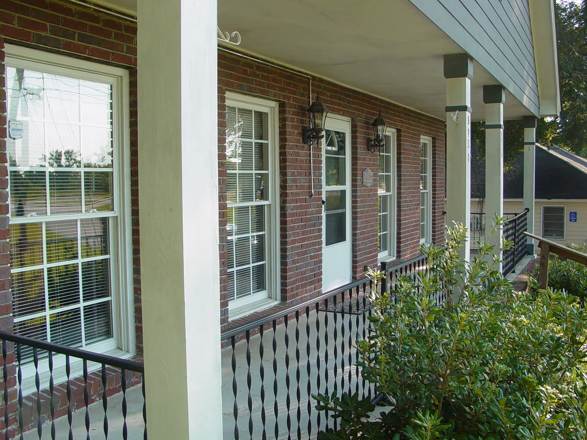 Covered brick front porch with white columns, windows, a doorway and a metal railing.