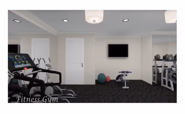Interior view of a fitness gym with exercise equipment including treadmills, stationary bikes, dumbbells, and exercise balls. The room has white walls, a black speckled floor, a wall-mounted TV, and ceiling lights.