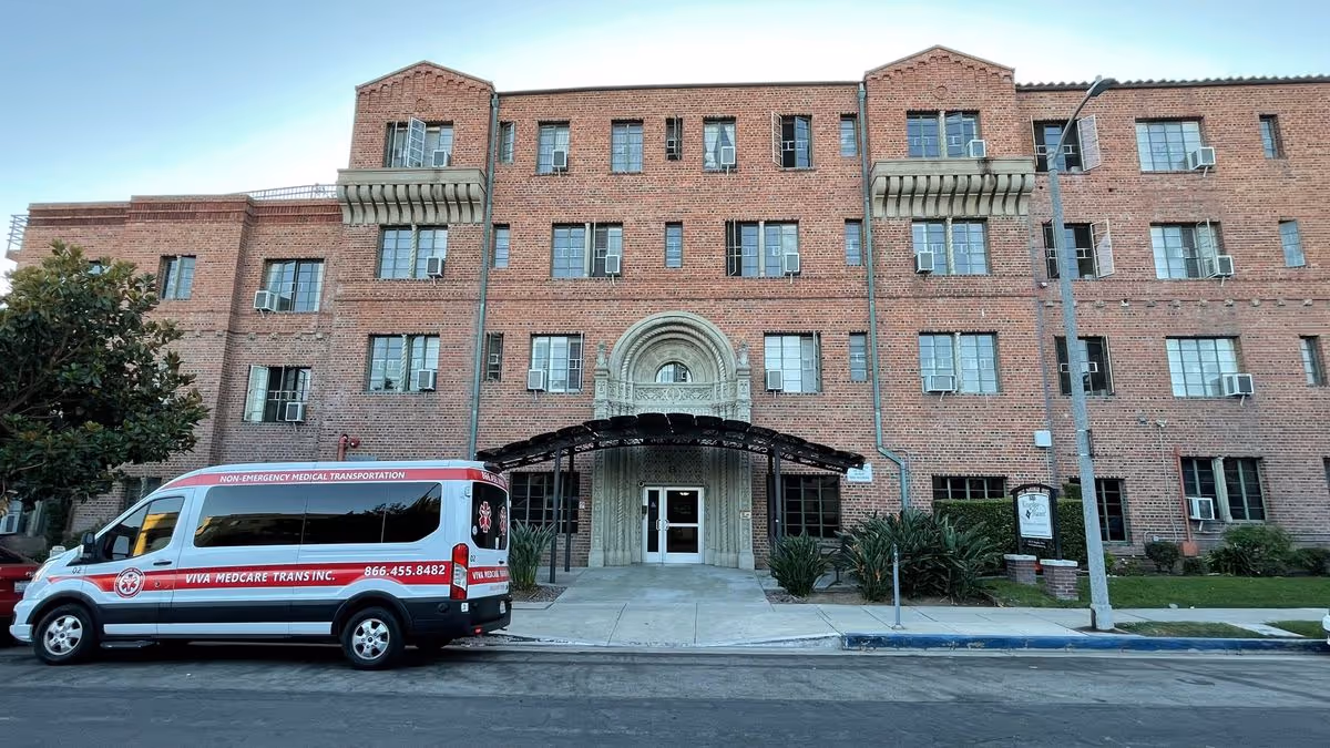 Four-story red brick building front with an ornate arched entrance and a parked medical transport van at the curb.