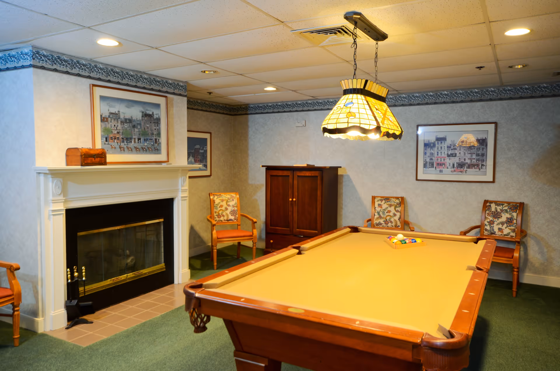 A cozy game room with a billiards table, hanging lamp, fireplace, and chairs.