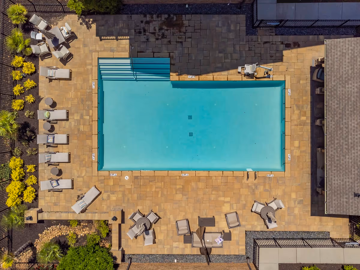 Aerial view of a rectangular outdoor swimming pool surrounded by lounge chairs, tables, and a tiled deck.
