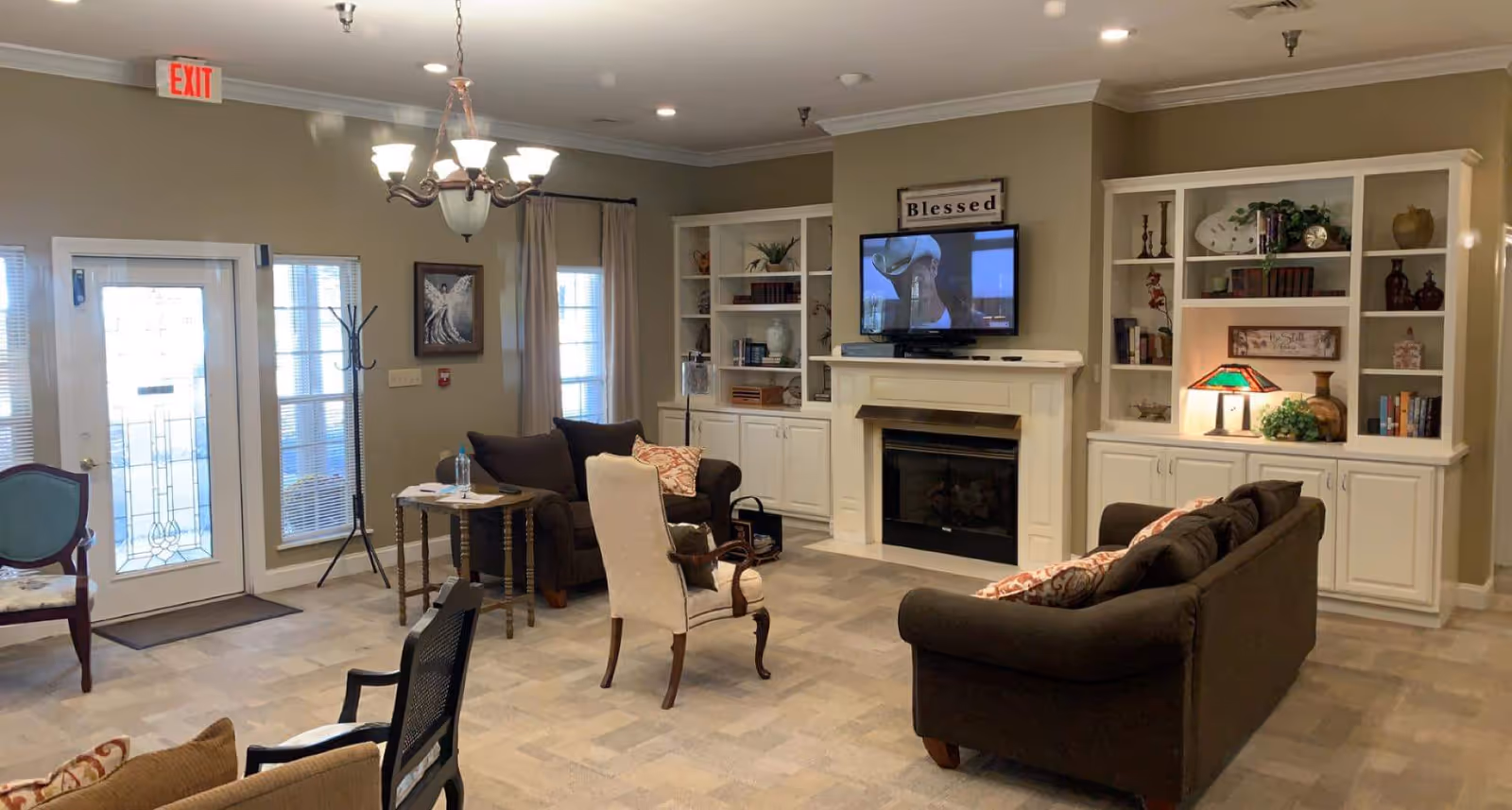 Comfortable common living room with sofas and armchairs, built-in bookshelves flanking a fireplace and TV, and a glass entry door.