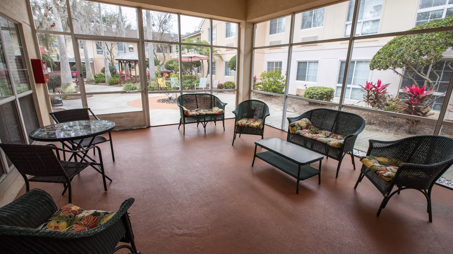 Screened-in patio/sunroom with wicker seating, small tables, and a view of a landscaped courtyard.