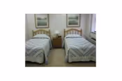 Small bedroom with two twin beds separated by a nightstand and lamps, with framed pictures above each bed.