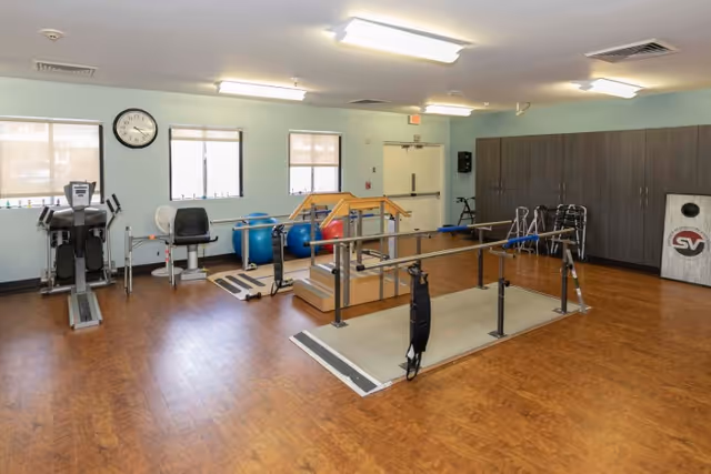 Rehabilitation therapy room with parallel bars, exercise machines, walkers, and exercise balls.