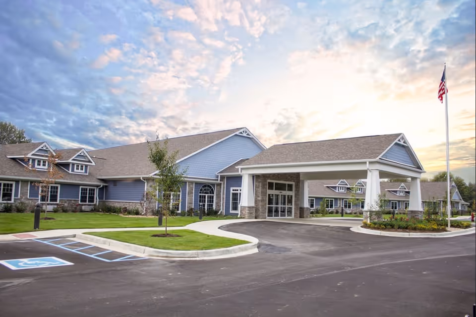 Front of a single-story healthcare facility with a covered porte-cochere, landscaped grounds, handicap parking spaces, and an American flag.