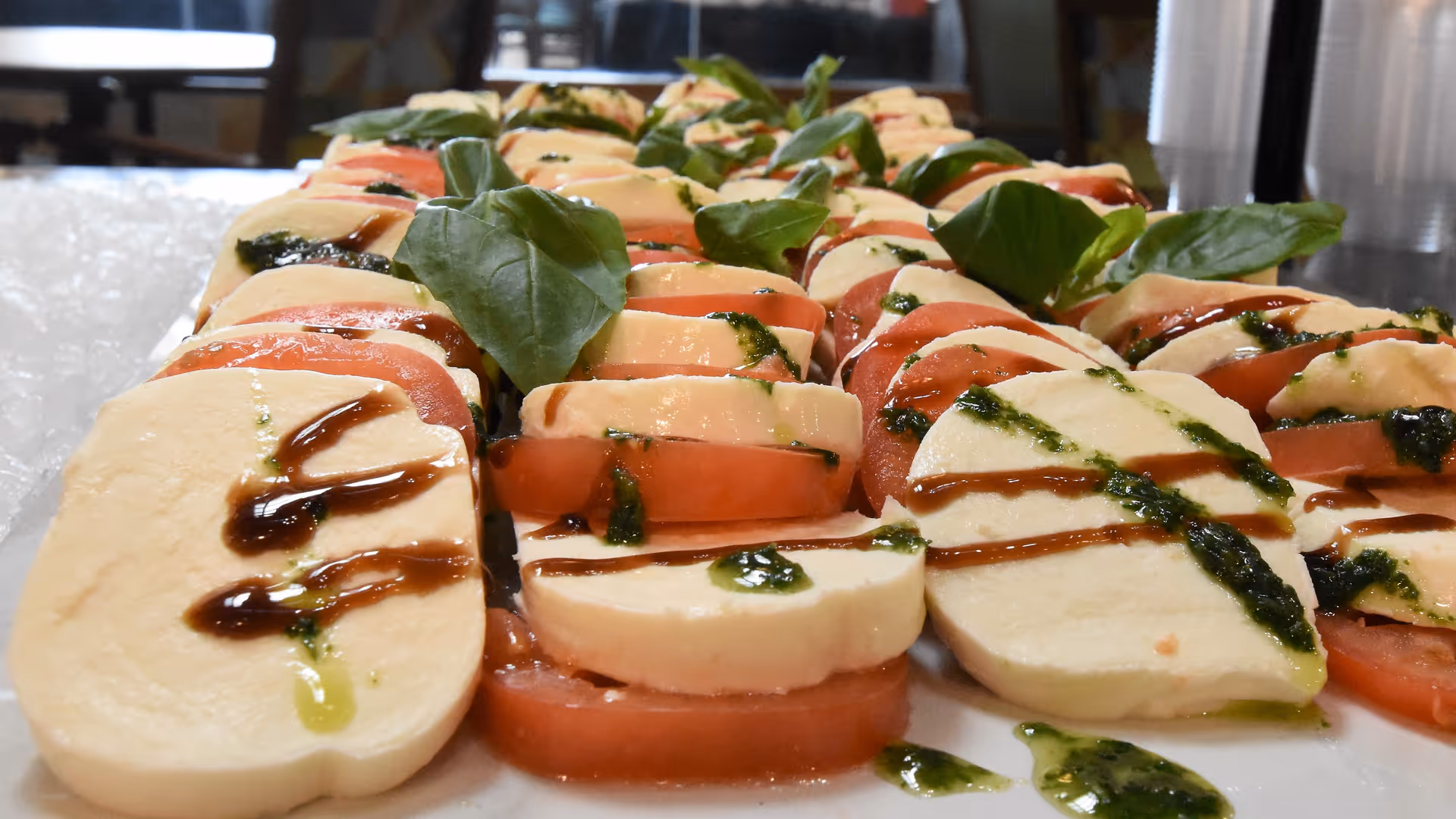 Close-up of sliced tomato and mozzarella caprese salad with basil and balsamic drizzle arranged on a serving platter.