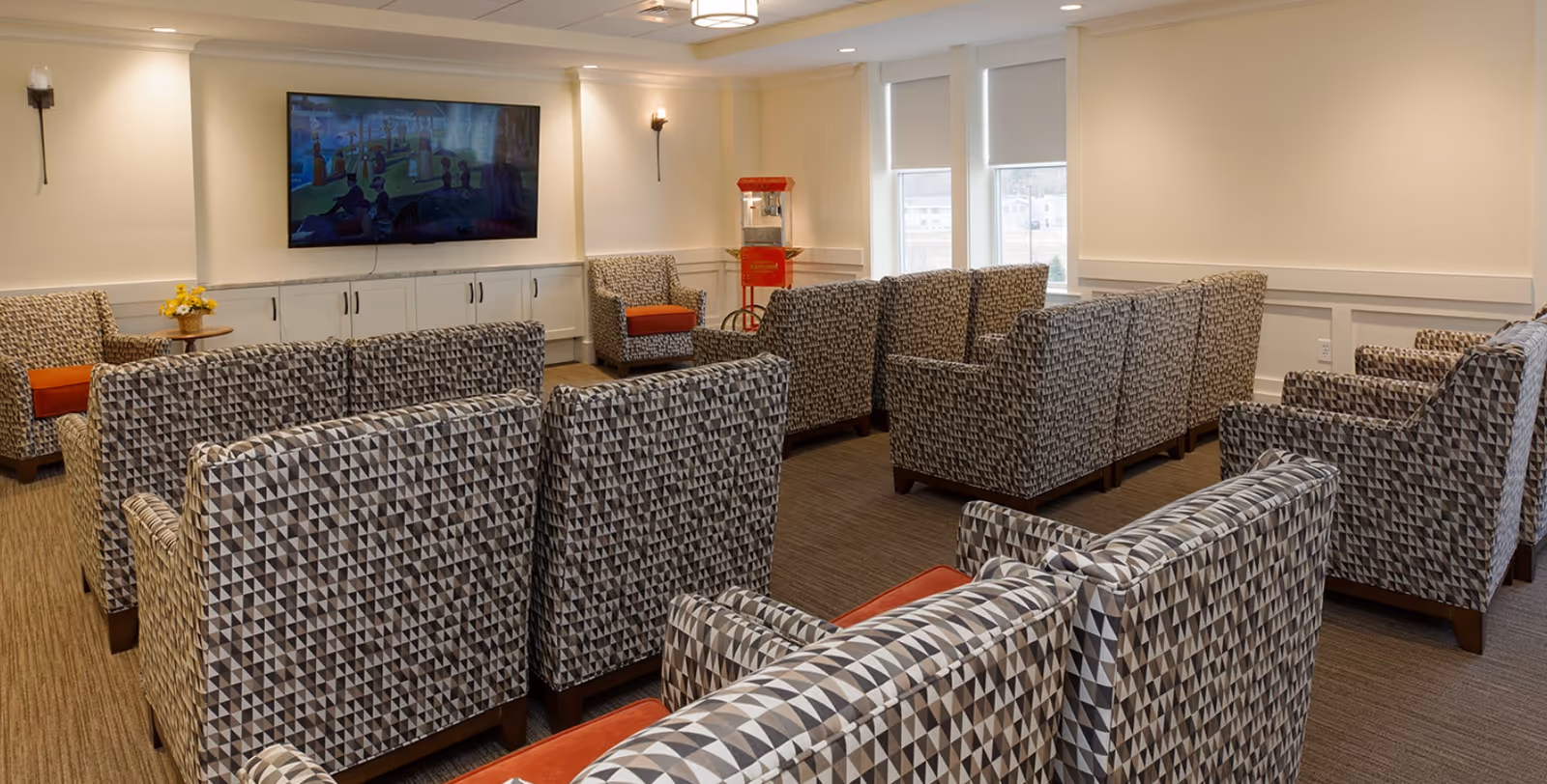 A seating area with patterned armchairs arranged theater-style facing a wall-mounted TV and a red popcorn machine.