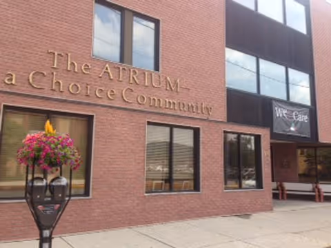 Front exterior of The ATRIUM - a Choice Community brick building with windows, an entrance, and a hanging flower basket.