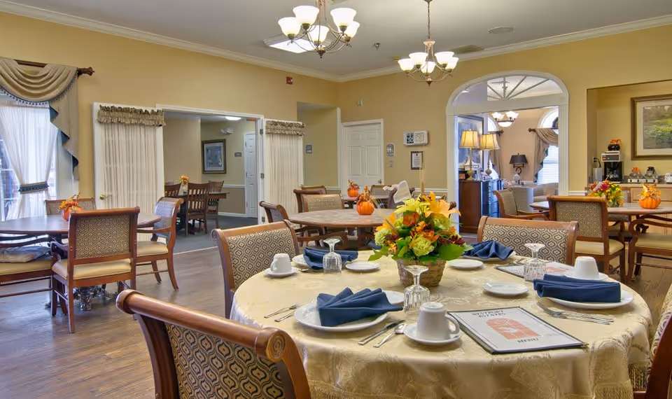 Bright dining room with round tables set with plates, napkins, glassware and floral centerpieces.