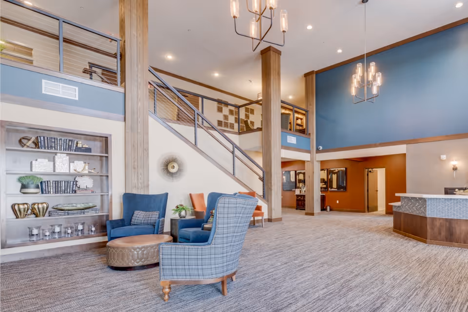 Spacious two-story lobby with seating area, staircase, bookshelves, and a reception desk.