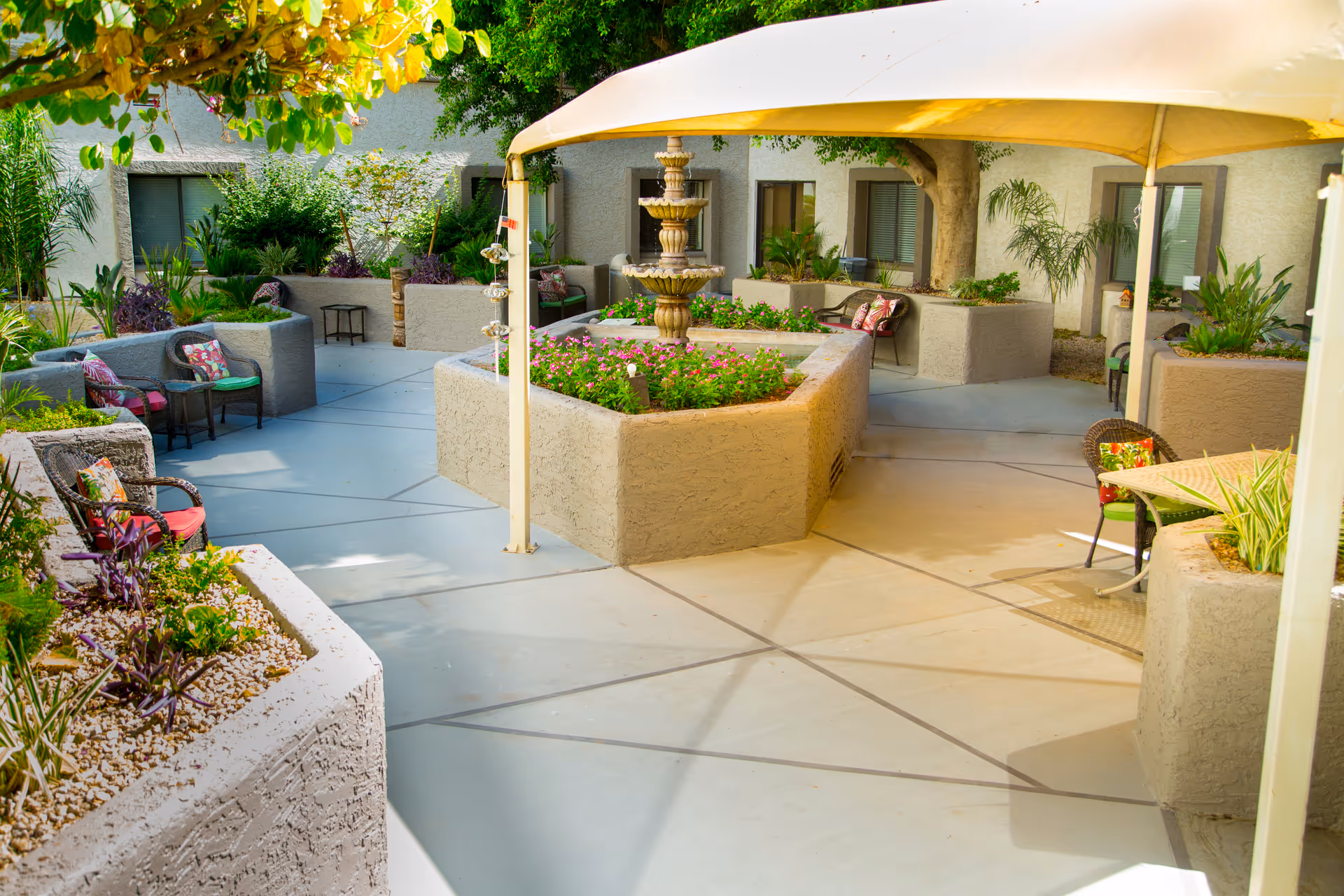 Shaded courtyard with a central tiered fountain, raised planter beds, and multiple seating areas under a canopy.