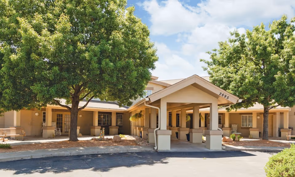 Front exterior of Brayden Park Assisted Living & Memory Care showing a covered entrance with columns, rocking chairs, and large trees.