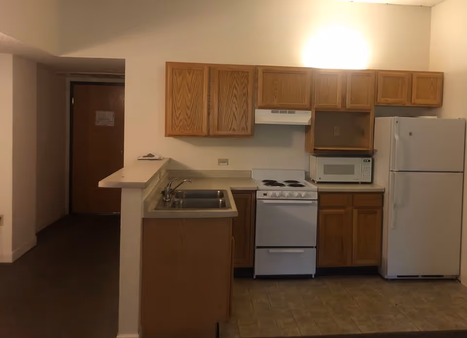 A compact kitchen with wood cabinets, a sink and breakfast bar, electric stove, microwave and refrigerator.