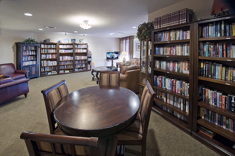 Community library/lounge with bookshelves, seating, and a round wooden table.