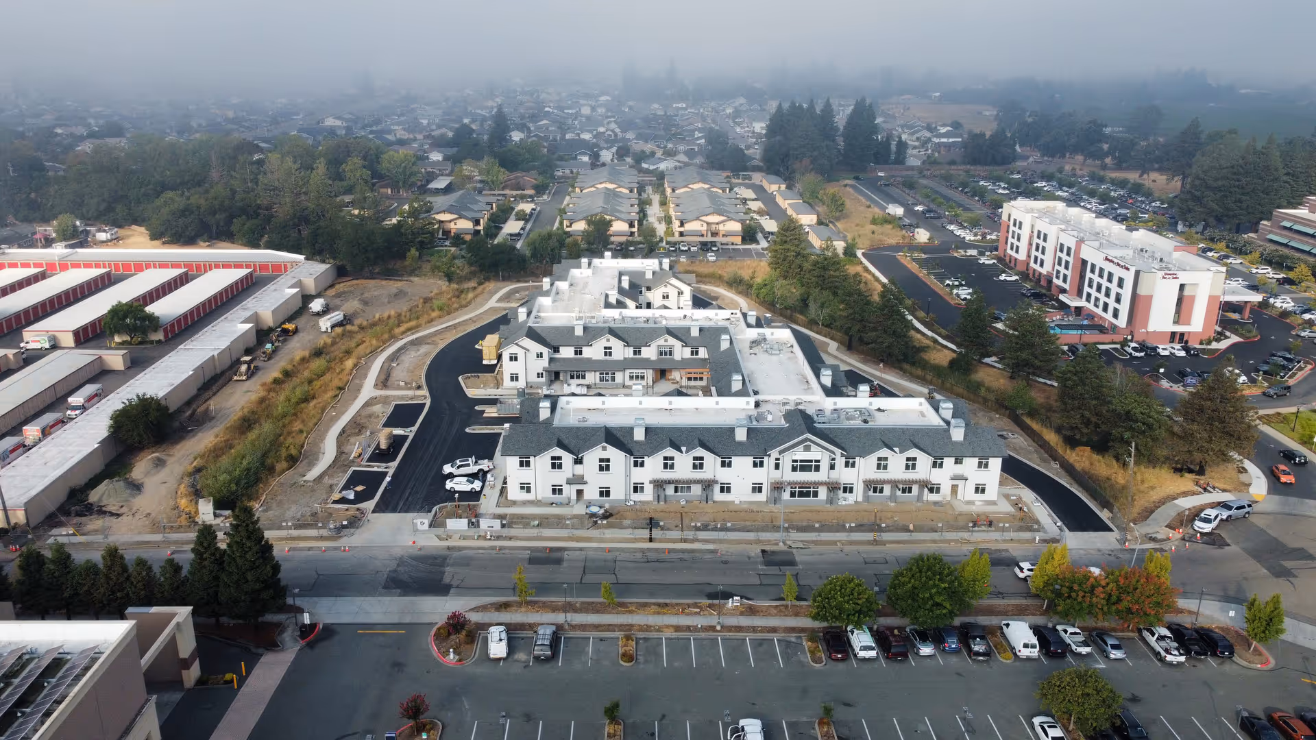 Aerial view of a large multi-wing senior living building with surrounding parking lots, roads, and nearby buildings.