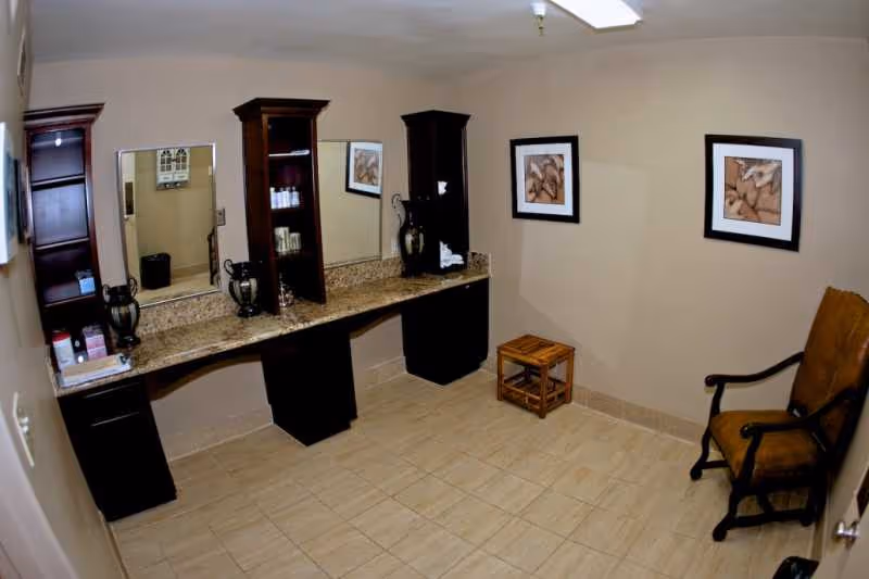 Interior vanity area with mirrors, cabinets, and a chair in a senior living facility.