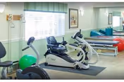 Rehabilitation exercise room with cardio equipment, therapy tables, exercise balls and a large mirror.