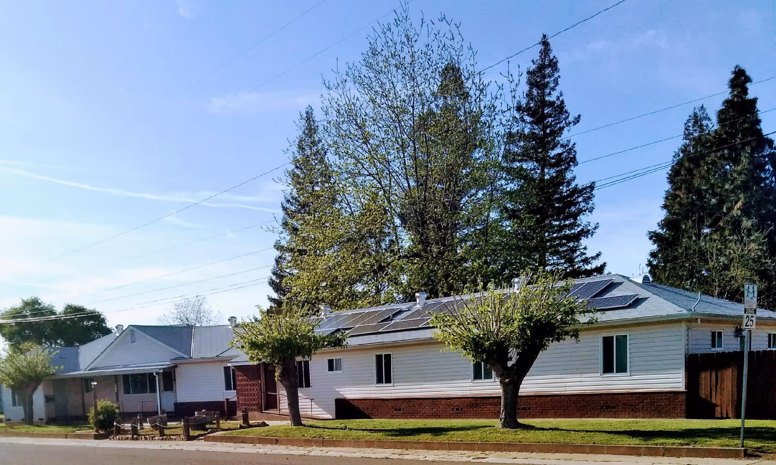Single-story guest home with solar panels on the roof, small trees and a grassy front yard beside a street.